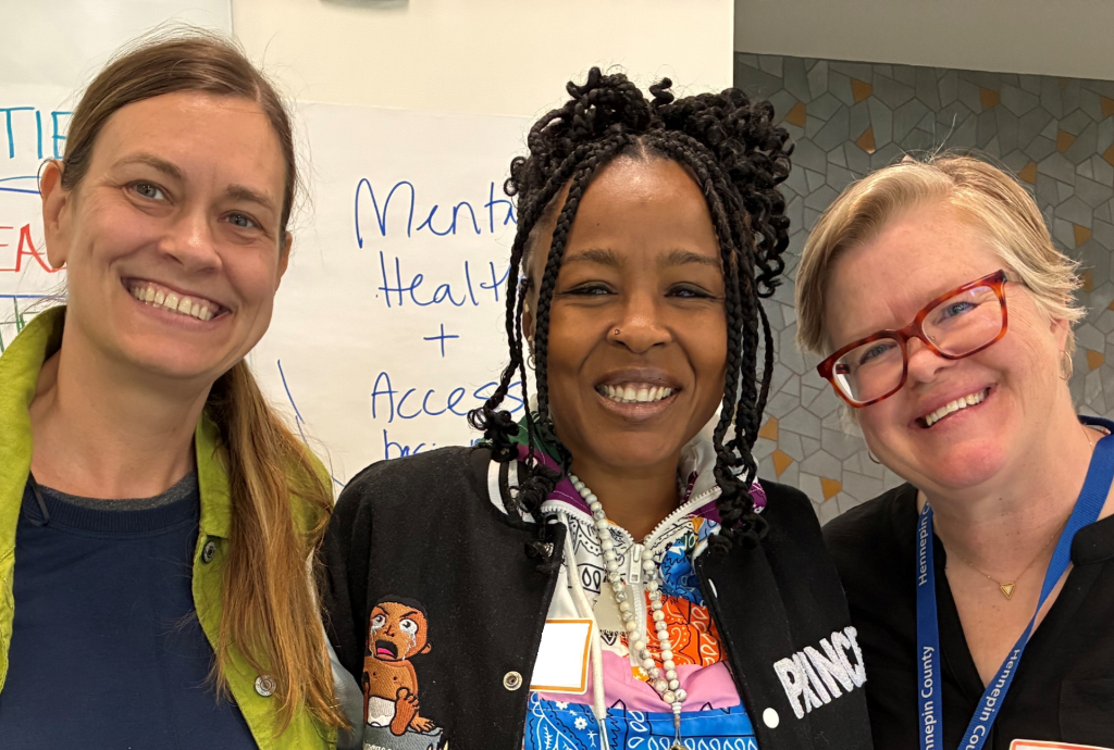 three people standing in front of posters at the community visioning session