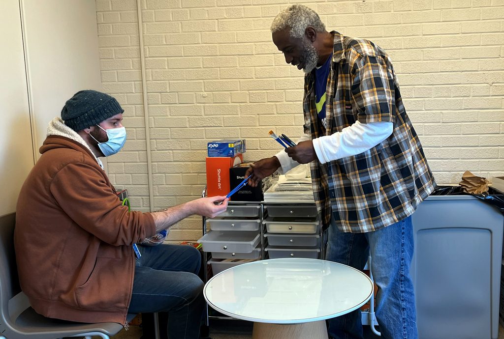 An Endeavors staff member hands paint brushes to a patient