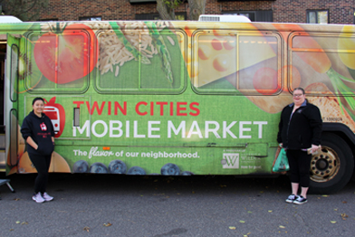 Two women standing in a front a Twin Cities Mobile Market bus